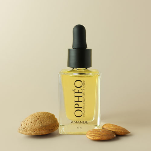 Flacon en verre avec pipette compte-goutte, contenant de l'huile végétale d'amande douce pour le visage. Devant le flacon se trouvent des amandes.