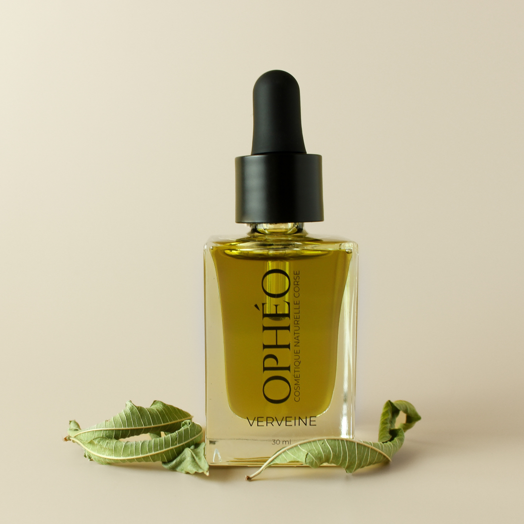 Huile Visage Verveine Apaisante 1 Flacon en verre avec pipette compte-goutte, contenant de un macérat de verveine citronnée pour le visage. Devant le flacon se trouvent des feuilles de verveine citronnée.